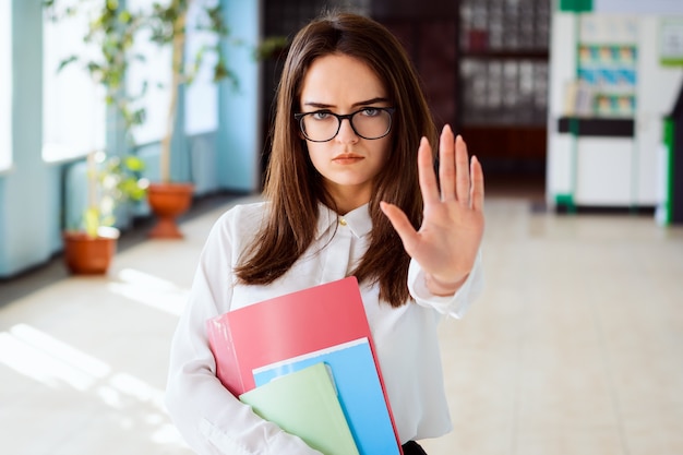 停止ジェスチャーを示す深刻な若い学生の女性の肖像画を閉じる