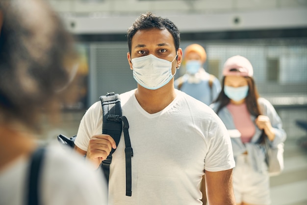 空港の写真カメラで見てポーズをとって肩にバックパックを背負ってカジュアルな服装で真剣にビジネスマンの肖像画をクローズアップ