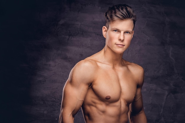 Close-up portrait of a sexy shirtless young man model with a muscular body and stylish haircut posing at a studio. Isolated on a dark background.