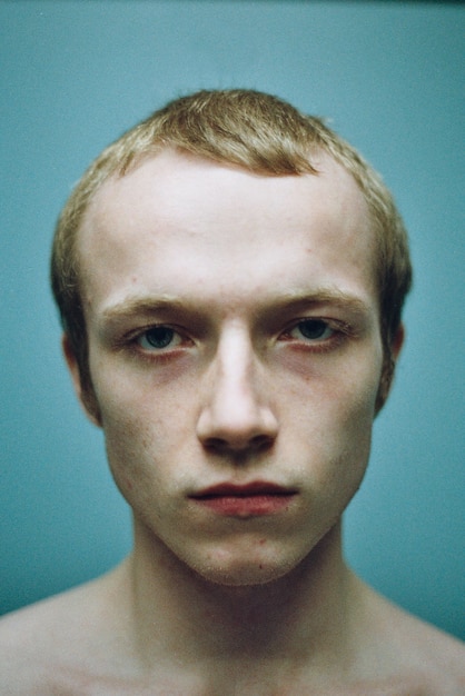 Close-up portrait of shirtless young man against turquoise background