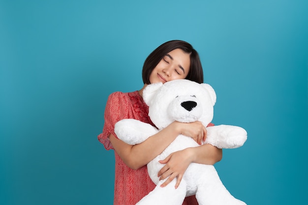 Close-up portrait of a sleeping  Asian woman with her eyes closed gently hugging a white Teddy bear