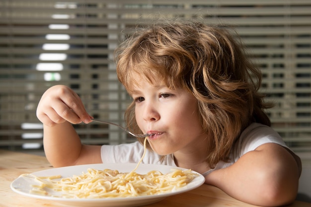 Close up portrait of a small blond boy eating pasta spaghetti Funny kids face