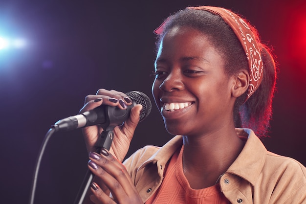 Close up portrait of smiling African-American woman singing to microphone while standing on stage, copy space