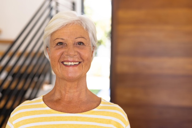 Крупным планом портрет улыбающейся двухрасовой пожилой женщины с короткими волосами у двери в доме престарелых. Вуд, счастливое, лицо, неизмененное, поддержка, концепция проживания для престарелых и выхода на пенсию.