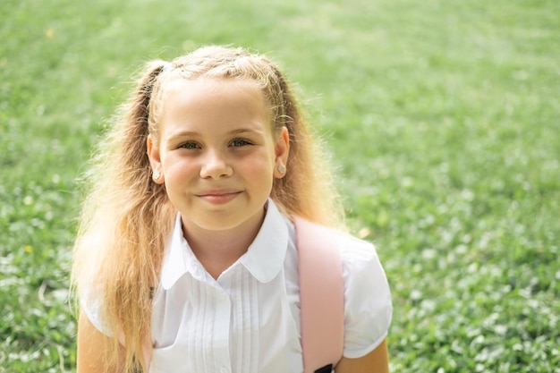 крупным планом портрет улыбающейся блондинки-школьницы в белой рубашке с розовым рюкзаком обратно в школу