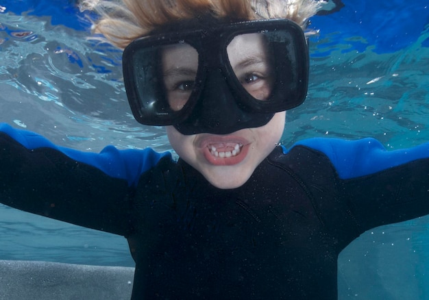 Foto ritratto ravvicinato di un ragazzo sorridente che indossa occhiali da sole che nuota sott'acqua