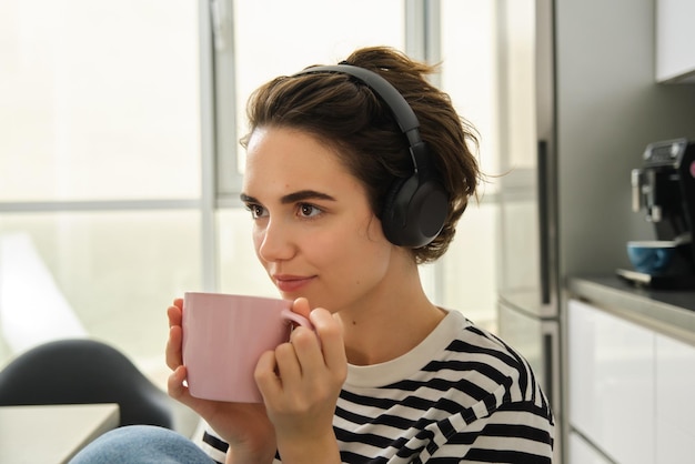 close up portrait of smiling brunette woman student drinks her tea and listens music or ebook in