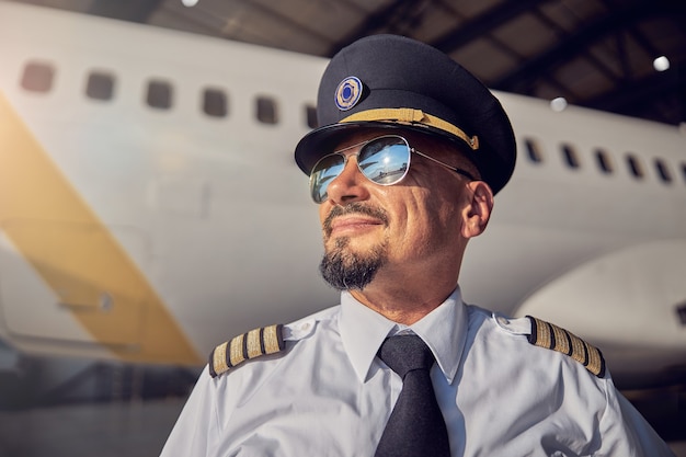 Ritratto ravvicinato di un uomo sorridente fiducioso in camicia bianca e cravatta scura in piedi di fronte all'aereo passeggeri