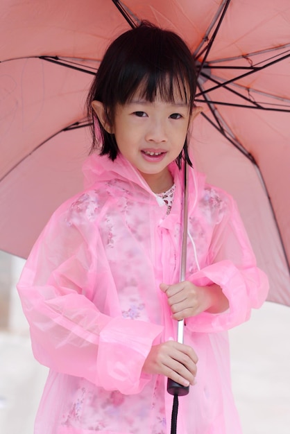 Photo close-up portrait of smiling cute girl wearing pink raincoat