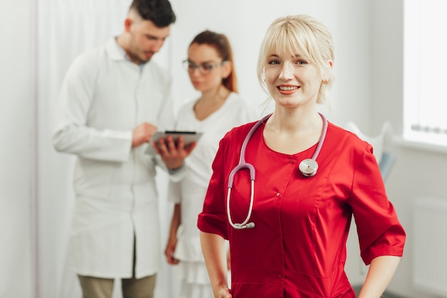 Foto ritratto del primo piano di un medico femminile sorridente in un'uniforme rossa con uno stetoscopio