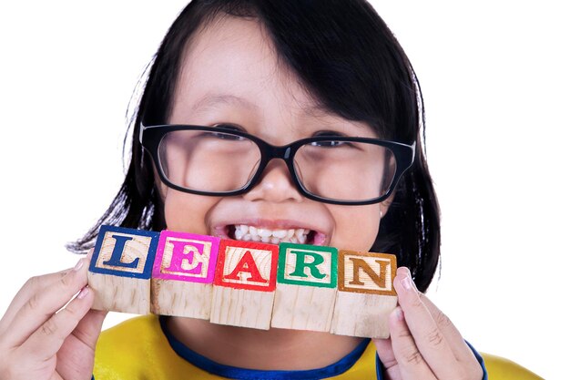 Photo close-up portrait of smiling girl holding toy blocks with learn text standing against white background