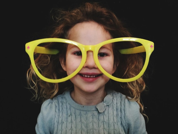 Close-up portrait of smiling girl wearing toy eyeglasses against black background