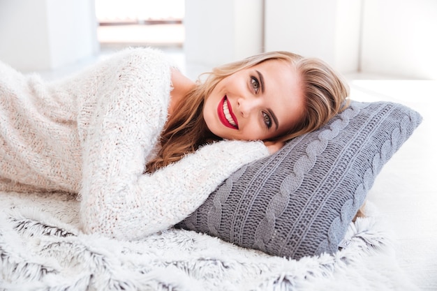 Close up portrait of a smiling happy woman laying on the pillow indoors