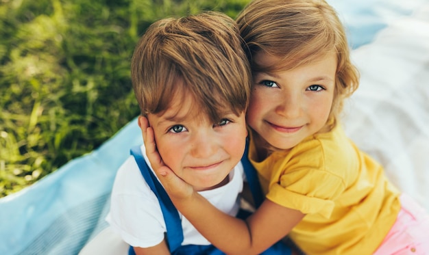 Close up portrait of smiling two children playing on the blanket outdoors Sister hugging her little brother in the park Kids having fun on sunlight