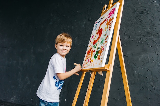 Макро портрет улыбающегося, белый трехлетний мальчик с кистью в руке. Концепция дошкольного образования, рисования, таланта, счастливой семьи или воспитания детей