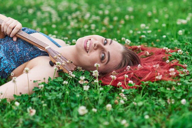 夏に草の上に横たわっている笑顔の女性の肖像画を閉じます。彼女の赤い髪は草の向こうに散らばっている。