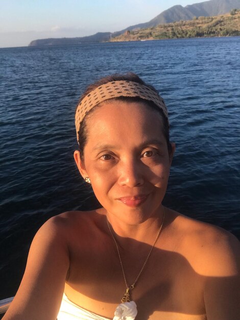 Close-up portrait of smiling woman standing against sea