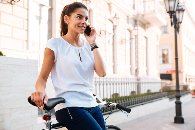 路上で自転車に乗ってスマートフォンで笑顔の若い女性の肖像画をクローズアップ