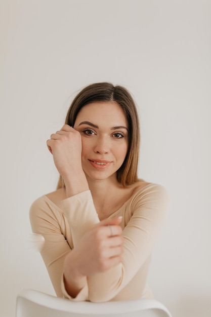 Ritratto ravvicinato di una bella ragazza alla moda con un sorriso romantico è in posa davanti alla fotocamera ragazza con i capelli chiari e il trucco nudo si tocca la guancia e guarda la fotocamera