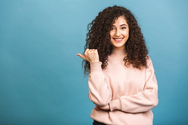 Close-up portrait of surprised pretty young woman in casual pointing finger, isolated on blue background.