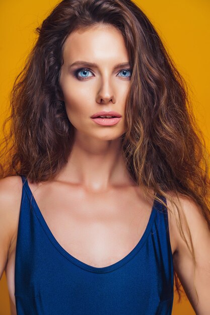 Close-up portrait of a tanned young woman with curly hair on yellow background.