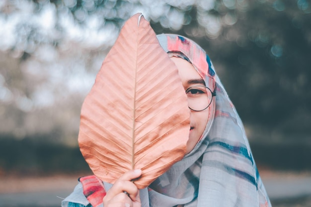 Close-up portrait of teenage girl covering face with dry leaf