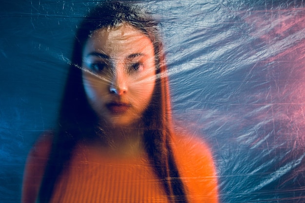 Close-up portrait of teenage girl seen through plastic while standing against wall