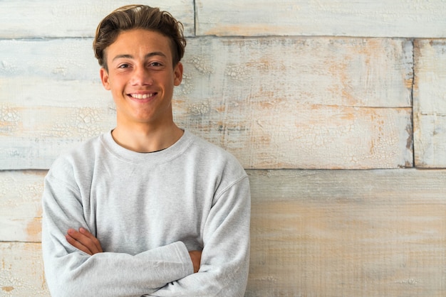 Photo close up and portrait of teenager or boy smiling and looking at the camera with a wooden background - beautiful and handsome man at home