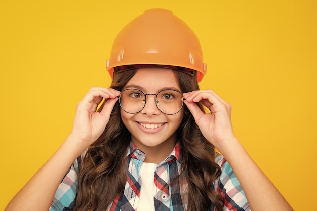 Close up portrait of teenager child builder in helmet Teenage girl on repairing work isolated on yellow background