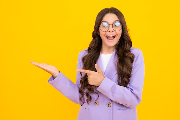 Close up portrait of teenager child girl showing at copy space pointing to ads advertising isolated over yellow background mock up copy space amazed teen girl excited expression