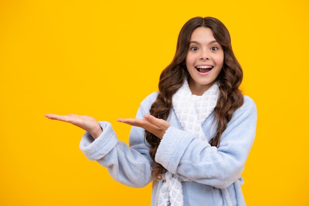 Close up portrait of teenager child girl showing at copy space pointing to ads advertising isolated over yellow background Mock up copy space