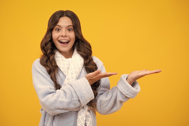 Close up portrait of teenager child girl showing at copy space pointing to ads advertising isolated over yellow background Mock up copy space