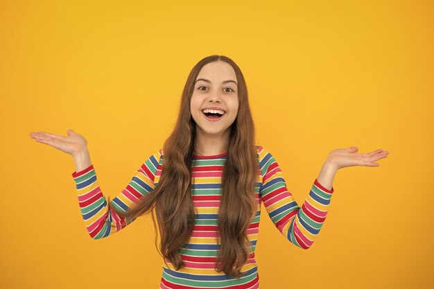 Close up portrait of teenager child girl showing at copy space pointing to ads advertising isolated over yellow background mock up copy space