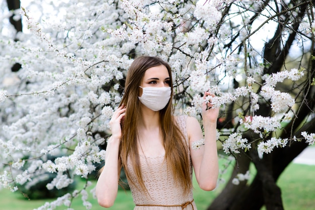 Close up portrait of tender female under a blossoming tree with a mask