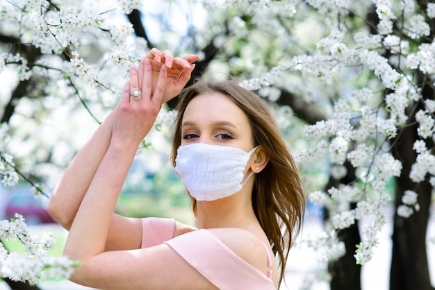 コロナウイルスからのマスクで開花桜の木の下で白いブラウスに柔らかい女の子の肖像画を閉じます。