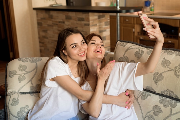 Close up portrait of two excited girlfriends with mobile phones, laughing. Happy joyful female friends resting at home, enjoying talks, having fun.