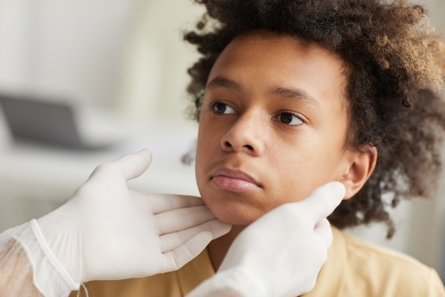 Close up portrait of unrecognizable doctor examining neck of African-American boy during consultation in clinic