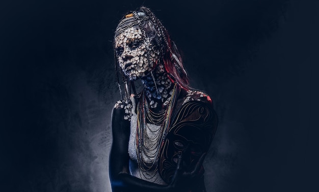 Close-up portrait of a witch from the indigenous African tribe, wearing traditional costume. Make-up concept. Isolated on a dark background.