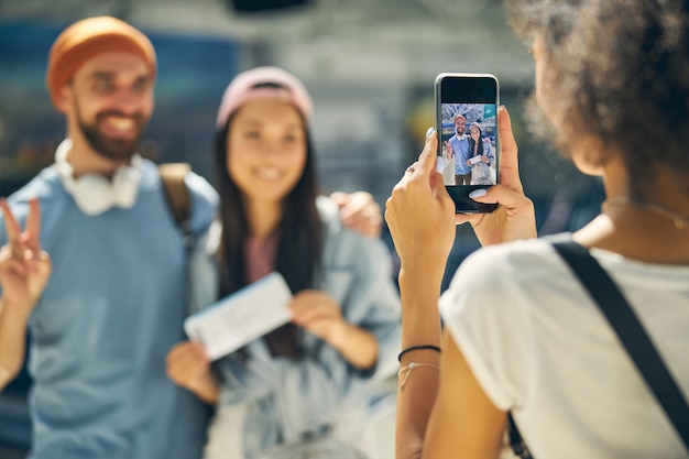 Close up portrait of woman taking photo in modern mobile phone for two young people in airport