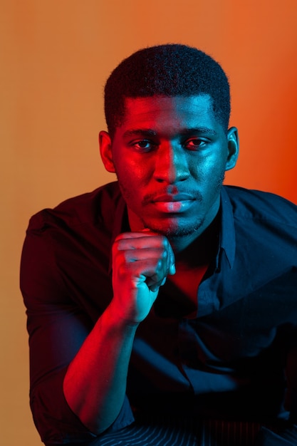 Close up portrait of a young african american man on orange neon  wall.