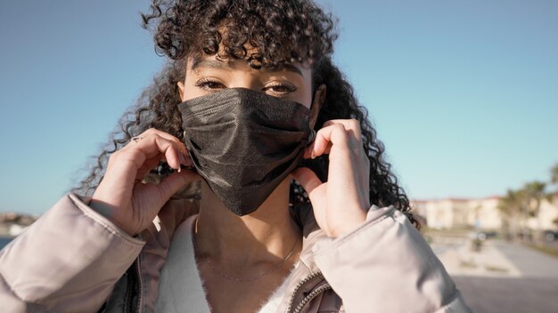 Foto primo piano ritratto di giovane donna afroamericana mentre indossa una maschera nera per evitare l'infezione da coronavirus.