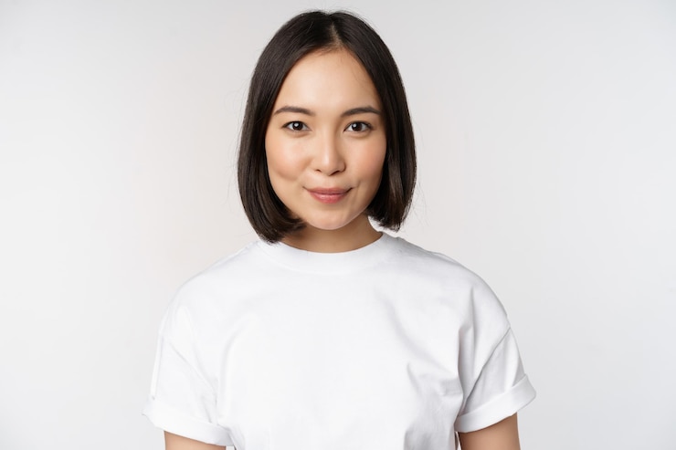 Photo 笑顔で幸せそうな白い背景を探しているtシャツを着てカメラを見て若いアジアの女性の肖像画をクローズアップ