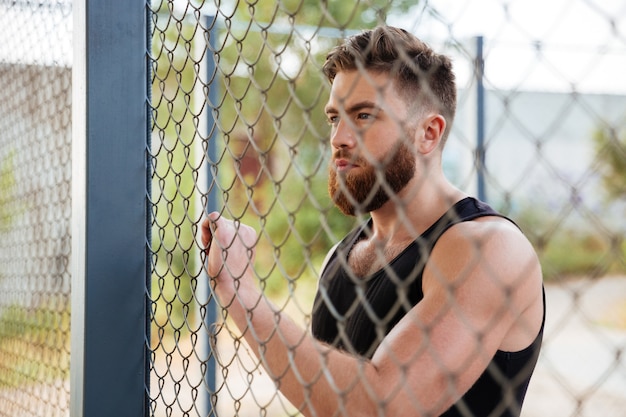 Close up portrait of young bearded man looking through metal urban fence outdoors