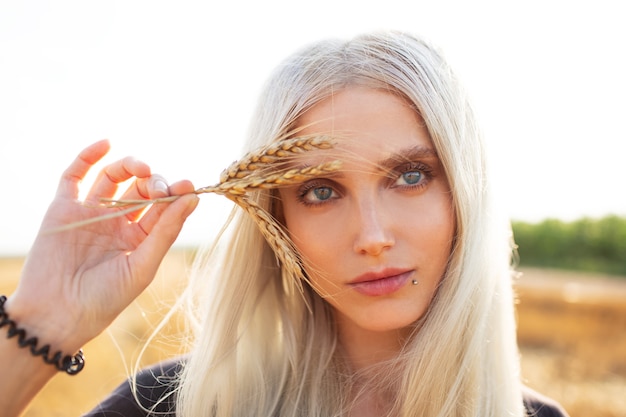 Close-up portrait of young beautiful blonde girl holding some wheat spikes.