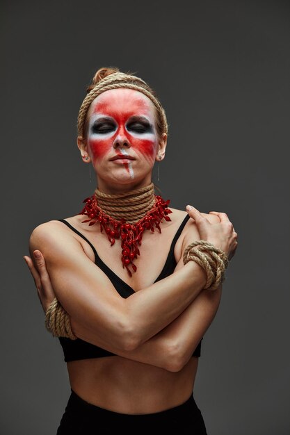 Close up portrait of young beautiful girl with colorful face painting Halloween professional makeup neck and hands are wrapped with ropes Victim Concept