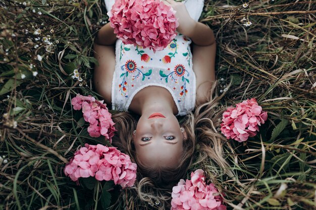 Foto chiuda sul ritratto di giovane bella ragazza che si trova sull'erba con i piccoli fiori rosa intorno alla sua testa