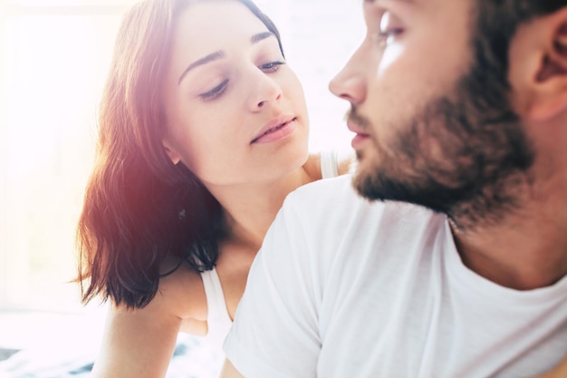 Close up portrait of young beautiful tender couple in love while them are sitting on bed and kissing, hugging and relaxing together. Love, relationships, family and St. Valentines day