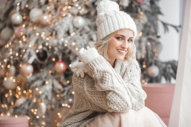 Close up portrait of young beautiful woman on Christmas scene. Smiling girl with perfect skin near the Christmas tree.
