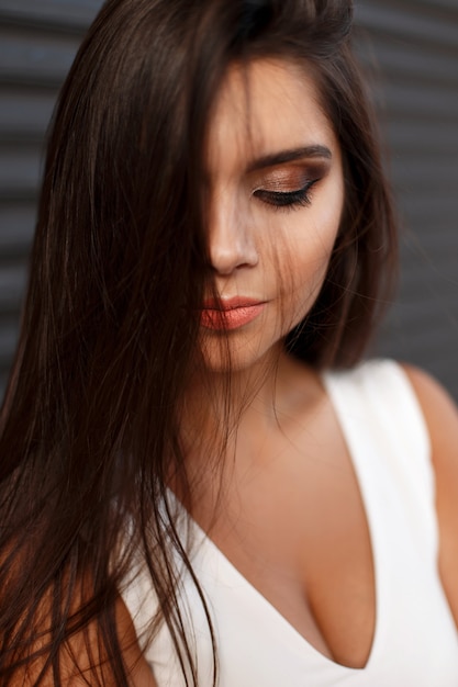 Close-up portrait of a young beautiful woman with makeup in white dress on a dark background