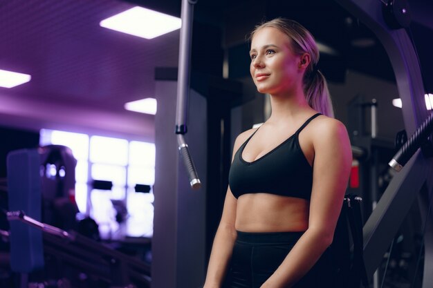 Close up portrait of a young blonde woman in sport bra in a dark gym